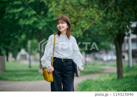 パソコンと手帳を手に持ち歩く若い女性 パソコンと手帳を手に持ち歩く若い女性 114323040