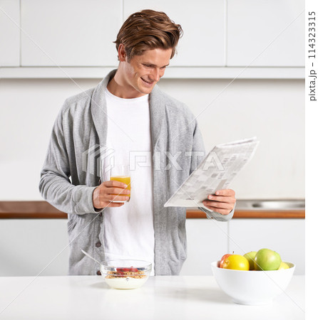 Breakfast, juice and man with newspaper in kitchen for information at modern apartment. Nutrition, cereal and young male person drinking healthy beverage and reading public journalism at home. 114323315