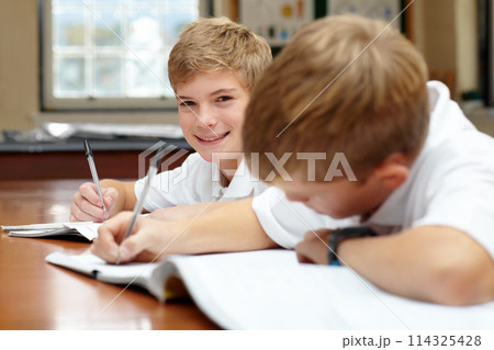 Happy students, classroom and writing in books for education, thinking mindset or children on scholarship. Boys, school kids or learning with creative idea on desk, studying and reading work in class 114325428