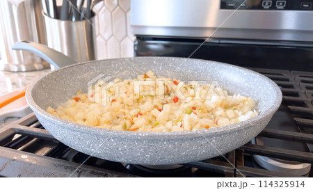 A frying pan on a gas stove sizzles with diced potatoes and colorful bits of red and green peppers, showcasing a delicious and simple home-cooked side dish in the making. 114325914