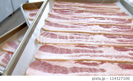 Neatly arranged raw bacon strips on a baking tray, prepared for cooking, capturing the fresh, uncooked look of this popular breakfast ingredient before it turns crispy and golden. 114327100