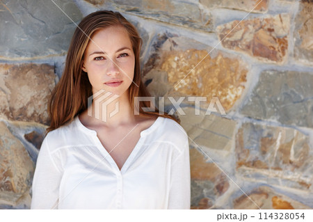 Woman, portrait and relax by stone wall in home with confidence, pride and casual outfit on weekend. Person, face and smile for holiday, vacation or peaceful getaway with shirt, good mood and calm 114328054