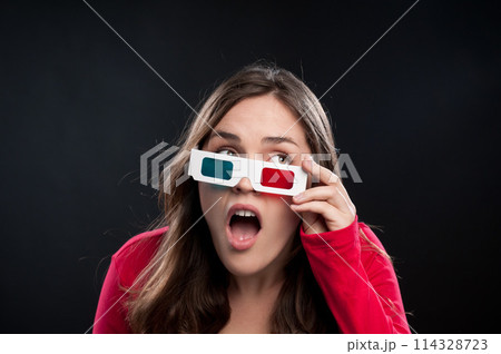 Woman, 3d glasses and surprise for watching movie, shocked or surreal in black studio background. Female person, wow and futuristic with color lens eyewear in cinema for mystery, film or mockup Woman, 3d glasses and surprise for watching movie, shocked or surreal in black studio background. Female person, wow and futuristic with color lens eyewear in cinema for mystery, film or mockup 114328723