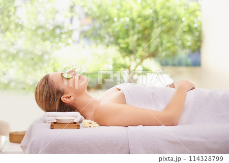 Woman, massage and spa with cucumber facial for skincare treatment or wellness, detox or stress relief. Female person, eyes closed and calm on table at zen resort for luxury, peace or comfortable 114328799