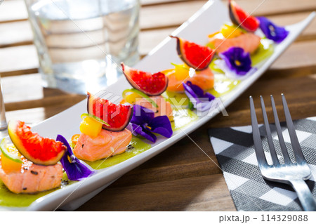 Ceviche from red trout on plate with cumquat, kiwi, figs and flower 114329088