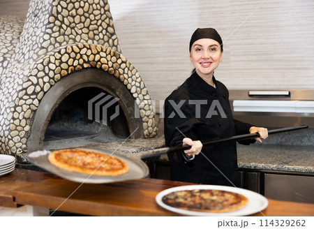 Smiling woman chef preparing pizza in restaurant 114329262