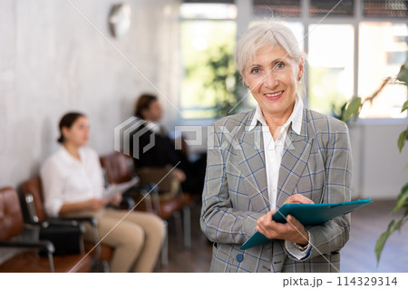 Elderly businesswoman writing tasks and instructions in office lobby Elderly businesswoman writing tasks and instructions in office lobby 114329314
