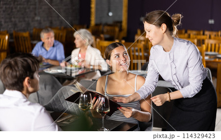 Waitress recommending dishes from menu to young couple Waitress recommending dishes from menu to young couple 114329423