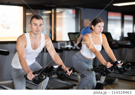 Portrait of concentrated man doing cardio training, cycling on stationary bike in gym. Sport and fitness concept Portrait of concentrated man doing cardio training, cycling on stationary bike in gym. Sport and fitness concept 114329463