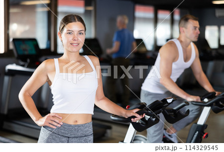 Young woman posing by exercise bike Young woman posing by exercise bike 114329545