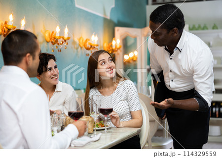 African american waiter talking with guests visiting restaurant African american waiter talking with guests visiting restaurant 114329559