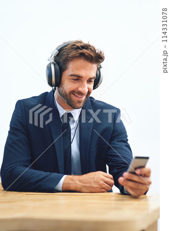 Headphones, office and businessman with mobile phone for social media, browsing internet or streaming music. Smile, smartphone and male person listening to radio, audio podcast or online ted talk Headphones, office and businessman with mobile phone for social media, browsing internet or streaming music. Smile, smartphone and male person listening to radio, audio podcast or online ted talk 114331078