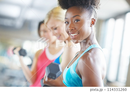 African athlete, dumbbell and portrait with smile in gym for workout, class and muscle growth. Woman, weight and happiness for exercise in fitness center for training, sport and strength development 114331260