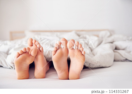 Feet, bed and couple in blanket with sleep for relax on honeymoon with getaway for togetherness and love in room. Toes, rest and intimacy vacation with duvet in house on weekend with comfort Feet, bed and couple in blanket with sleep for relax on honeymoon with getaway for togetherness and love in room. Toes, rest and intimacy vacation with duvet in house on weekend with comfort 114331267