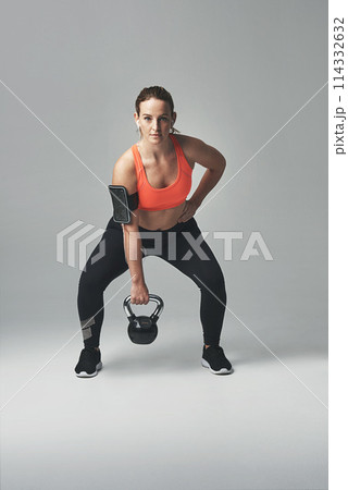 Woman, portrait and kettlebell in studio, squat and confidence for workout or training. Female person, athlete and weightlifting for muscle progress on gray background, earphones and body challenge 114332632
