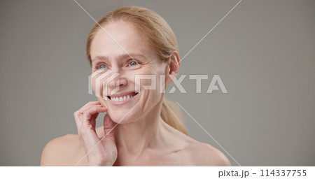 Real people - age, beauty, health and dry skin care concept - beautiful mature Caucasian middle aged woman in her 50s touching her face skin with a slight smile and good mood Real people - age, beauty, health and dry skin care concept - beautiful mature Caucasian middle aged woman in her 50s touching her face skin with a slight smile and good mood 114337755