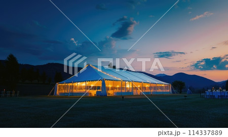 Outdoor wedding reception at twilight with illuminated tent and guests 114337889