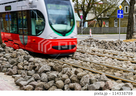A modern low-floor electric tram runs on newly replaced tracks, unfinished paving works 114338789