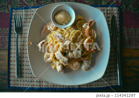 Overhead view of a plate of creamy shrimp pasta topped with parmesan cheese on a patterned tablecloth Overhead view of a plate of creamy shrimp pasta topped with parmesan cheese on a patterned tablecloth 114341297