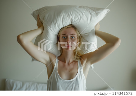 Young woman covering ears with pillow because of noise. 114341572