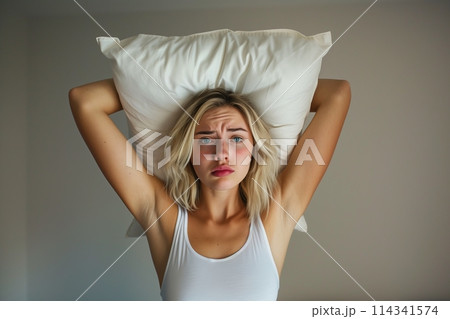 Young woman covering ears with pillow because of noise. 114341574