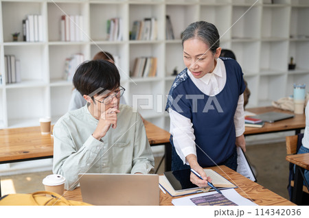 A mature Asian female teacher helping and explaining difficult math problems to her student. 114342036