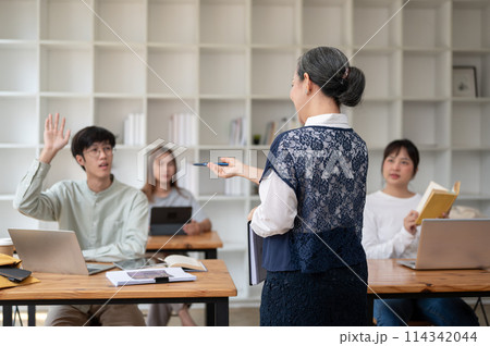 A back view image of a teacher professor giving a lecture to her students in the classroom. A back view image of a teacher professor giving a lecture to her students in the classroom. 114342044
