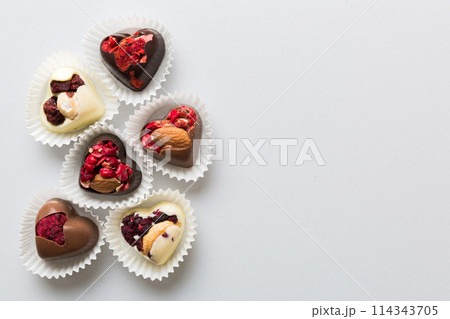 chocolate sweets in the form of a heart with fruits and nuts on a colored background. top view with space for text, holiday concept chocolate sweets in the form of a heart with fruits and nuts on a colored background. top view with space for text, holiday concept 114343705