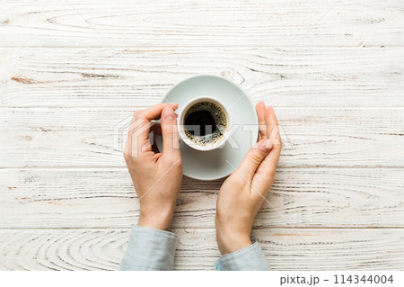 Minimalistic style woman hand holding a cup of coffee on Colored background. Flat lay, top view cappuccino cup. Empty place for text, copy space. Coffee addiction. Top view, flat lay 114344004