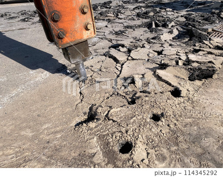 Heavy machine with demolition jackhammer is breaking asphalt on a city street. The operation of the drilling the road surface 114345292