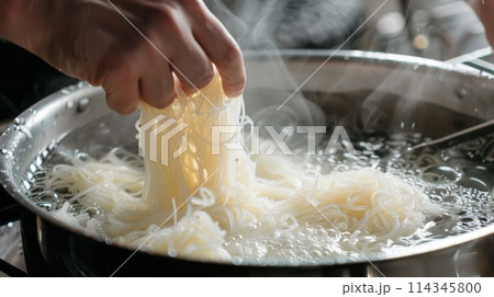 Close-up of man's hand cooking shirataki noodle in pan. 114345800