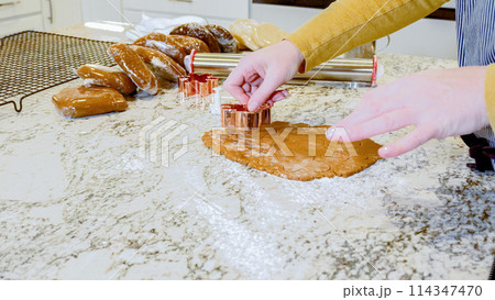 Using various festive cookie cutters, we're cutting out charming gingerbread cookies from the rolled dough on the sleek marble counter, bringing holiday cheer to the modern kitchen. Using various festive cookie cutters, we're cutting out charming gingerbread cookies from the rolled dough on the sleek marble counter, bringing holiday cheer to the modern kitchen. 114347470