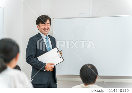 塾・学校の教室で小学生・中学生の子供に勉強を教える男性講師・教師 塾・学校の教室で小学生・中学生の子供に勉強を教える男性講師・教師 114348139