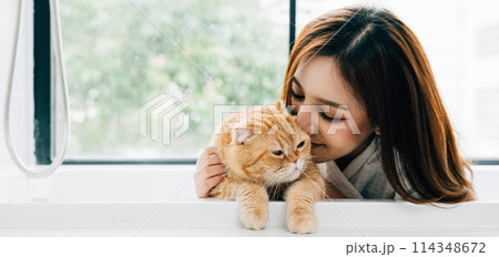 Enjoying a luxurious bath, a woman's contented smile reflects her deep connection with her Scottish Fold cat, exemplifying the bond between owner and pet in their cozy bathroom. 114348672