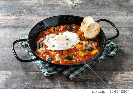 Eggplant and egg, onions, peppers, served in frying pan on wooden table, Vegetable pisto manchego with tomatoes, zucchini Eggplant and egg, onions, peppers, served in frying pan on wooden table, Vegetable pisto manchego with tomatoes, zucchini 114348804