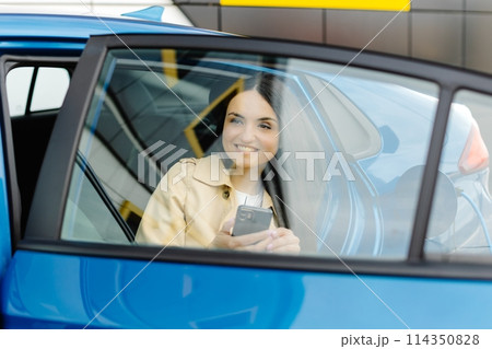 Business lady sitting inside charging electric car and using modern smartphone. Technology and transport concept. Business lady sitting inside charging electric car and using modern smartphone. Technology and transport concept. 114350828