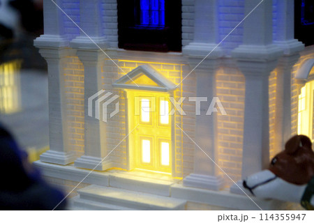 Prototype printed on 3D printer brick building with columns and glowing windows. Model of building with white and brown color, windows with light shining, created by 3D printer from molten plastic 114355947