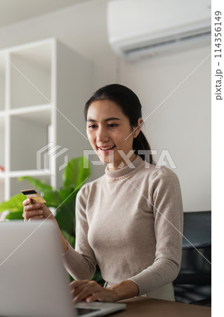 A woman is sitting at a desk with a laptop and a credit card in her hand A woman is sitting at a desk with a laptop and a credit card in her hand 114356149