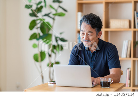 リビングで株式投資をするシニア男性。 114357114