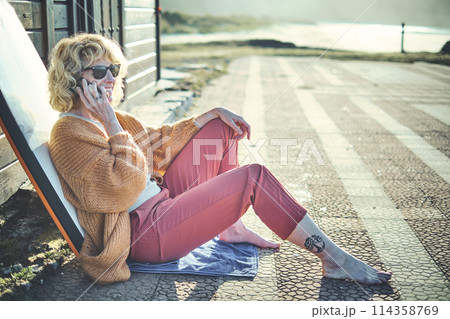 Young mature blonde woman outdoor with a bodyboard talking with a mobile phone. 114358769