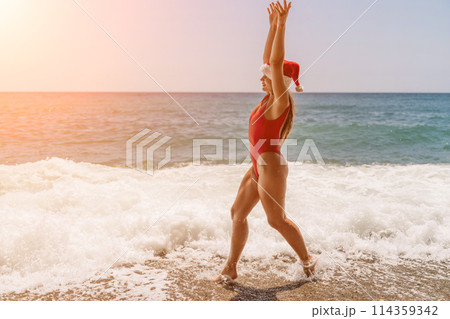 A woman in Santa hat on the seashore, dressed in a red swimsuit. New Year's celebration in a hot country. 114359342