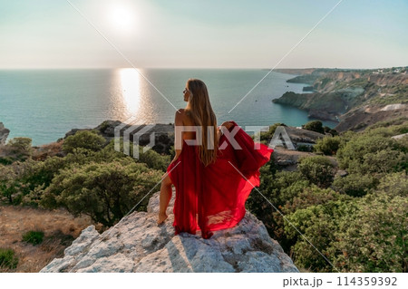 Woman sunset sea red dress, back view a happy beautiful sensual woman in a red long dress posing on a rock high above the sea on sunset. 114359392