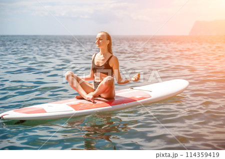 Woman sup sea. Sports girl on a surfboard in the sea on a sunny summer day. In a black bathing suit, he sits on a sapa in the sea. Rest on the sea. Woman sup sea. Sports girl on a surfboard in the sea on a sunny summer day. In a black bathing suit, he sits on a sapa in the sea. Rest on the sea. 114359419