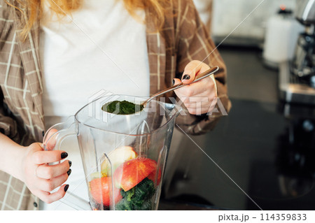 Close up woman adding spirulina or chlorella powder during making smoothie on the kitchen. Superfood supplement. Healthy detox vegan diet. Healthy dieting eating, weight loss program. Selective focus 114359833