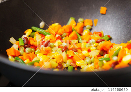 Spoon vigorously stirs a medley of vegetables in a sizzling pan, creating a symphony of colors and aroma. 114360680