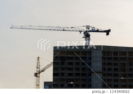 Construction cranes on top of a building under construction. The cranes are engaged in the construction work of the building. 114360682