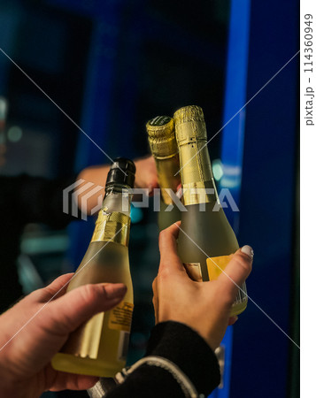 Close up of two hands holding bottles of champagne in the night club 114360949