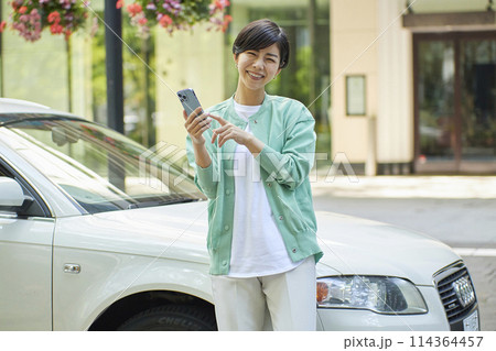 車の前でスマホを使用する若い女性 114364457