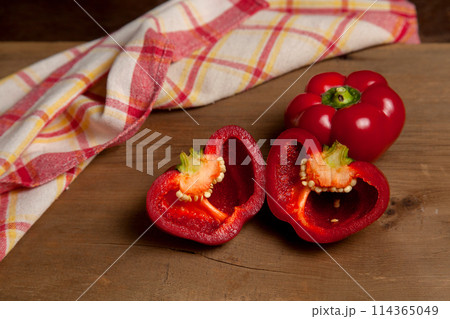 Whole and halves of red bell pepper on wooden background with red kitchen towel. . 114365049
