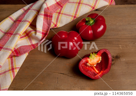 Two whole and halves of red bell pepper on wooden background with red kitchen towel. . 114365050